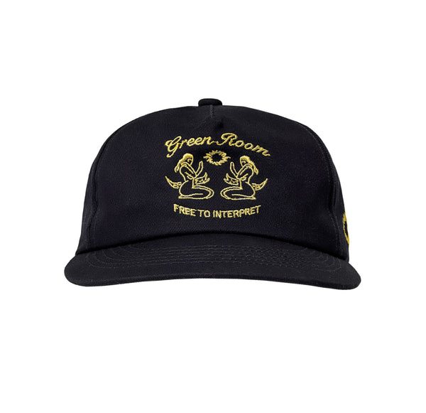 Schwarze Cap mit gelber Stickerei auf der Front, zeigt zwei einander zugewandte Meerjungfrauen mit stilisiertem Auge darüber und dem Schriftzug „Free to Interpret“ darunter.