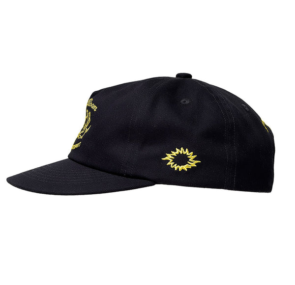 Linke Seite der Cap mit gelber Stickerei eines gezackten, abstrahierten Sonnensymbols.