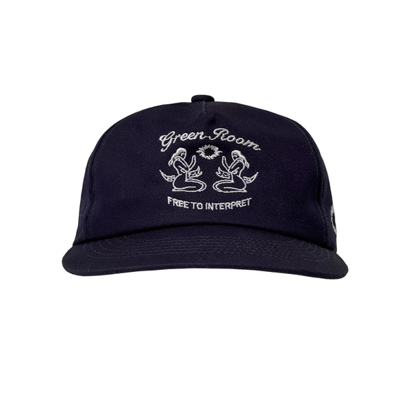 Dunkelblaue Cap mit weißer Stickerei zweier stilisierter Meerjungfrauen, die sich gegenüber sitzen. Darüber steht in geschwungener Schrift „Green Room“, darunter „FREE TO INTERPRET“. Flacher, gebogener Schirm.